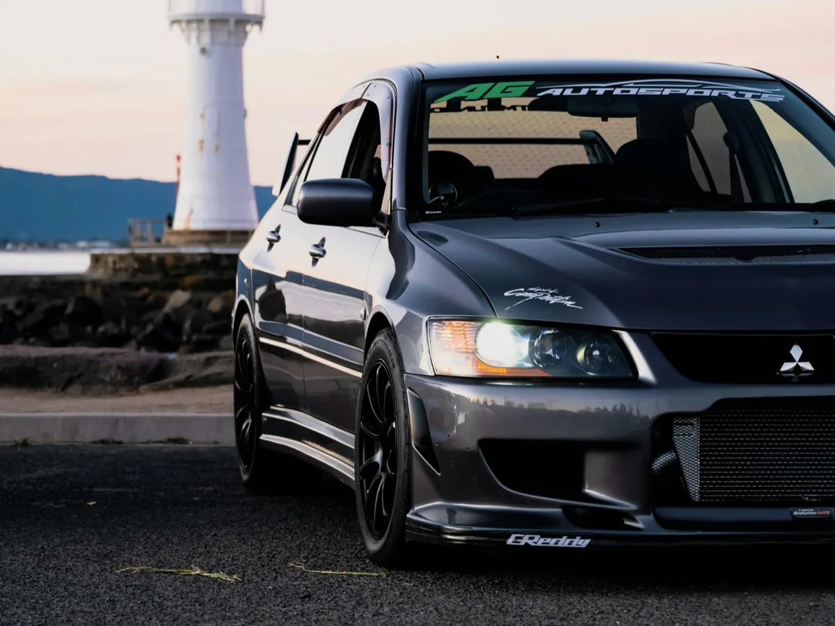 Grey Mitsubishi Lancer Evo by a lighthouse at dusk